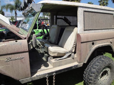 1993 Ford Taurus - A dusty Ford Bronco shows its interior with tan seats and a roll bar, parked outdoors with other vehicles visible.