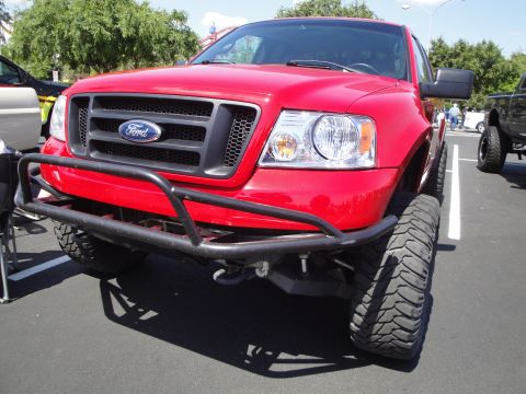 1993 Ford Taurus - A red Ford F-150 truck is parked in a lot, showing its front end and modified tires.