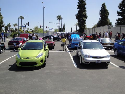 1993 Ford Taurus - A lime green hatchback is parked in a lot with several other vehicles and people milling around.
