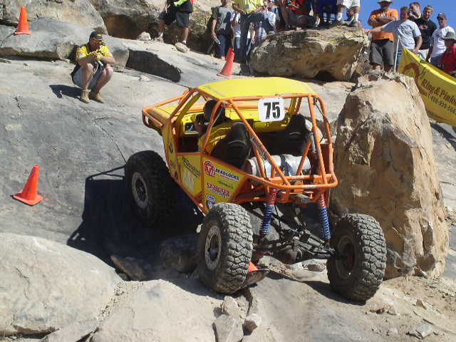 Yellow off-road buggy with orange roll cage and number 75 on the roof, climbing rocks