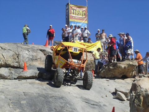 1979 Ford Bronco - A buggy competes in an off-road race with spectators gathered on the rocks above.