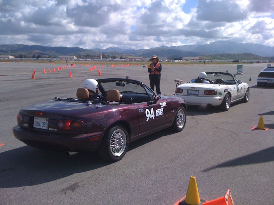 Maroon convertible sports car with racing numbers on the door, seen from the rear quarter