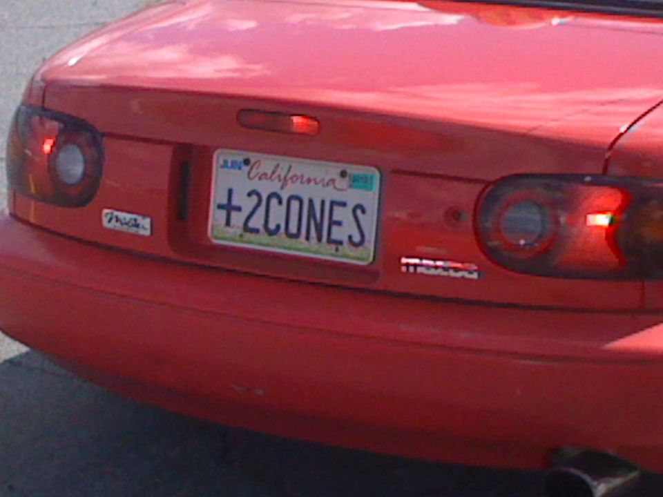 Red convertible with California plate +2CONES. Has 'Miata' badge on left and 'Mazda' badge on right