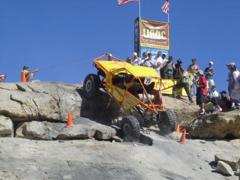 1979 Ford Bronco - A yellow off-road buggy with a prominent roll cage tackles a steep, rocky course during an event.