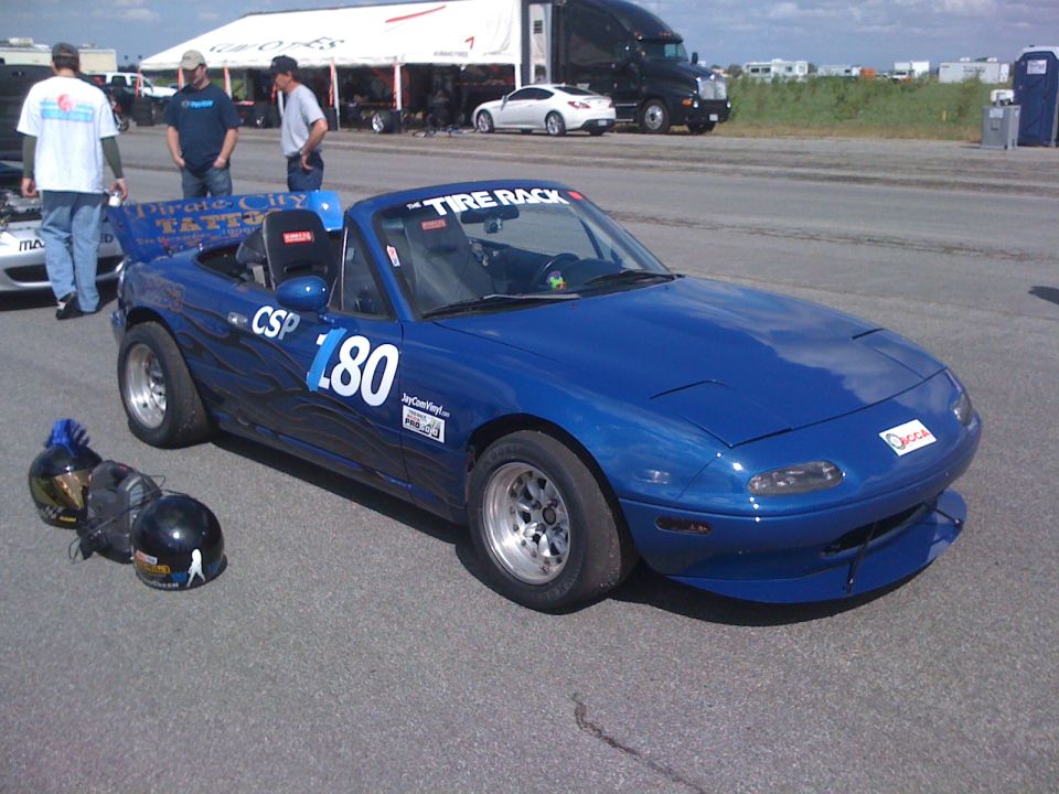 Blue NA Miata #L80 CSP autocross car with ghost flames and splitter, helmets on the ground