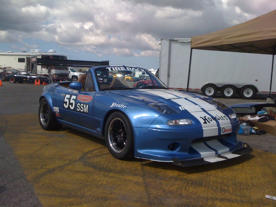 Blue NA Miata SSM #55 with white stripes, front splitter and pop-up headlights, three-quarter front view