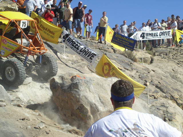 Yellow off-road buggy with number 75 on a rocky incline, kicking up dust