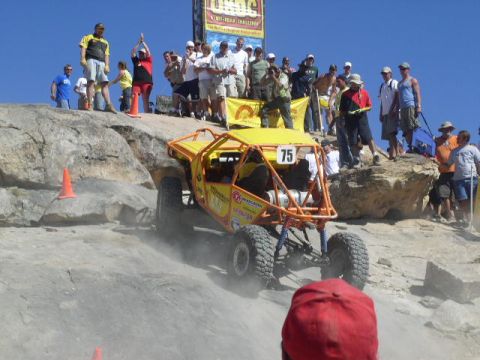 1979 Ford Bronco - A yellow off-road buggy navigates a challenging rocky terrain during an event, with spectators watching from the ridge above.