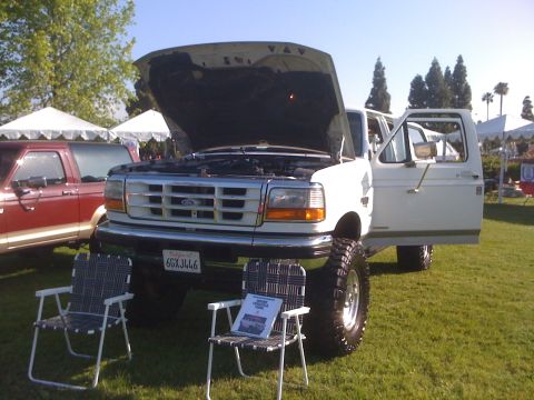 1996 Ford C-350 (Centurion Conversions) - A white Ford F-Series truck is displayed with its hood and driver's door open, parked on grass next to a red Ford Bronco.