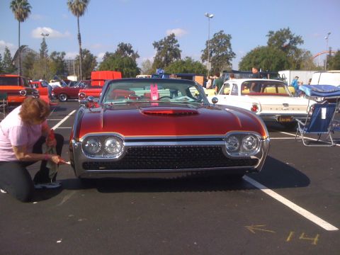 1996 Ford C-350 (Centurion Conversions) - A woman cleans the front tire of a red 1961 Ford Thunderbird at a car show.