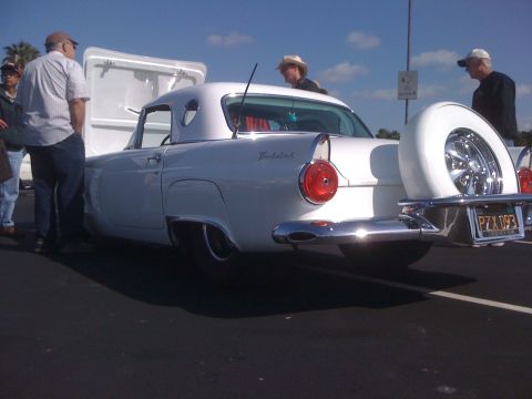 1996 Ford C-350 (Centurion Conversions) - A white classic car with a continental kit and spare tire is parked with its trunk open, while onlookers stand nearby.