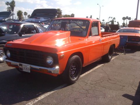 1996 Ford C-350 (Centurion Conversions) - This modified orange pickup truck features a prominent hood scoop and black wheels, with a Nevada license plate visible.