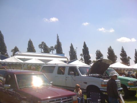 1996 Ford C-350 (Centurion Conversions) - Several vehicles are parked in a row under a sunny sky, with tents set up in the background.