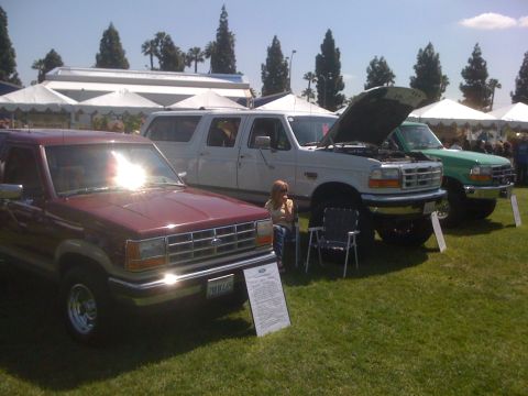 1996 Ford C-350 (Centurion Conversions) - A lineup of Ford trucks and SUVs, including a maroon Explorer and two larger trucks, one white and one green.