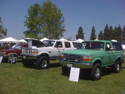 1996 Ford C-350 (Centurion Conversions) - A green Ford Bronco is parked on a grassy field next to other vehicles, with tents in the background.