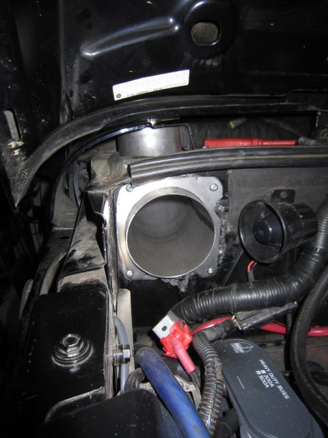 2008 Jeep Wrangler - Detail of a custom cold-air intake feed-through in an engine bay: a large-diameter aluminum tube passing through a bracket-mounted flange p…