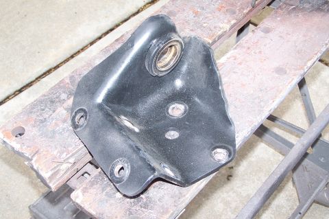 2000 Ford F-150 - A black metal bracket with a bearing is shown, resting on a workbench. The part has several bolt holes.