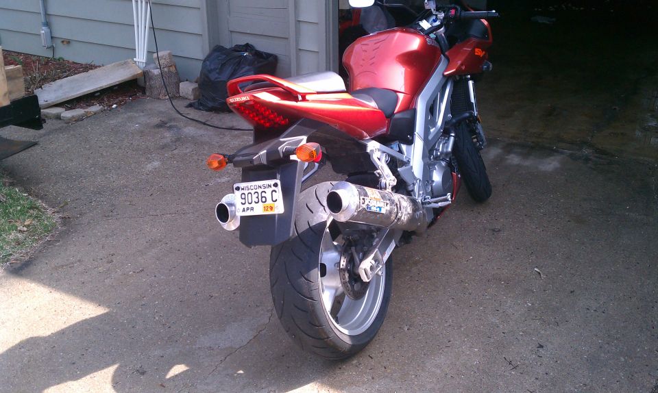 Red motorcycle parked on concrete, rear view showing dual exhaust and Wisconsin license plate