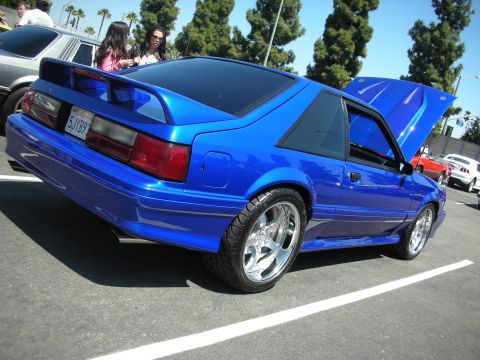 2004 Ford Crown Victoria - A blue coupe with a spoiler and custom wheels is parked at an outdoor event.