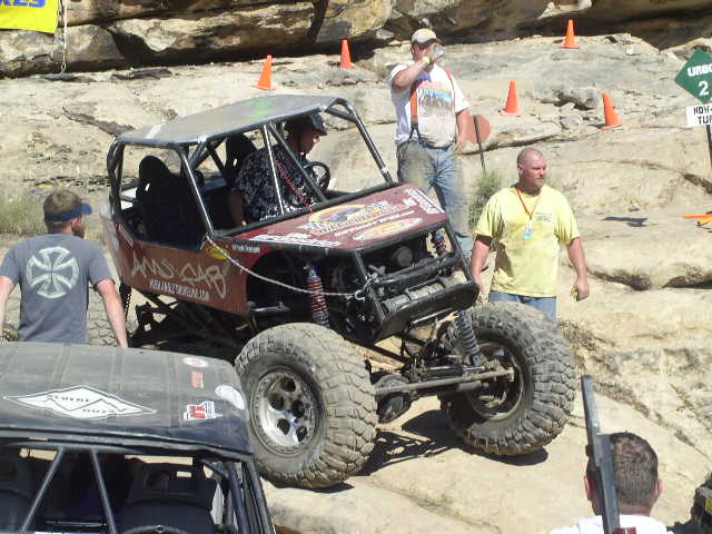 Red off-road buggy with roll cage and large tires, parked on rocky terrain