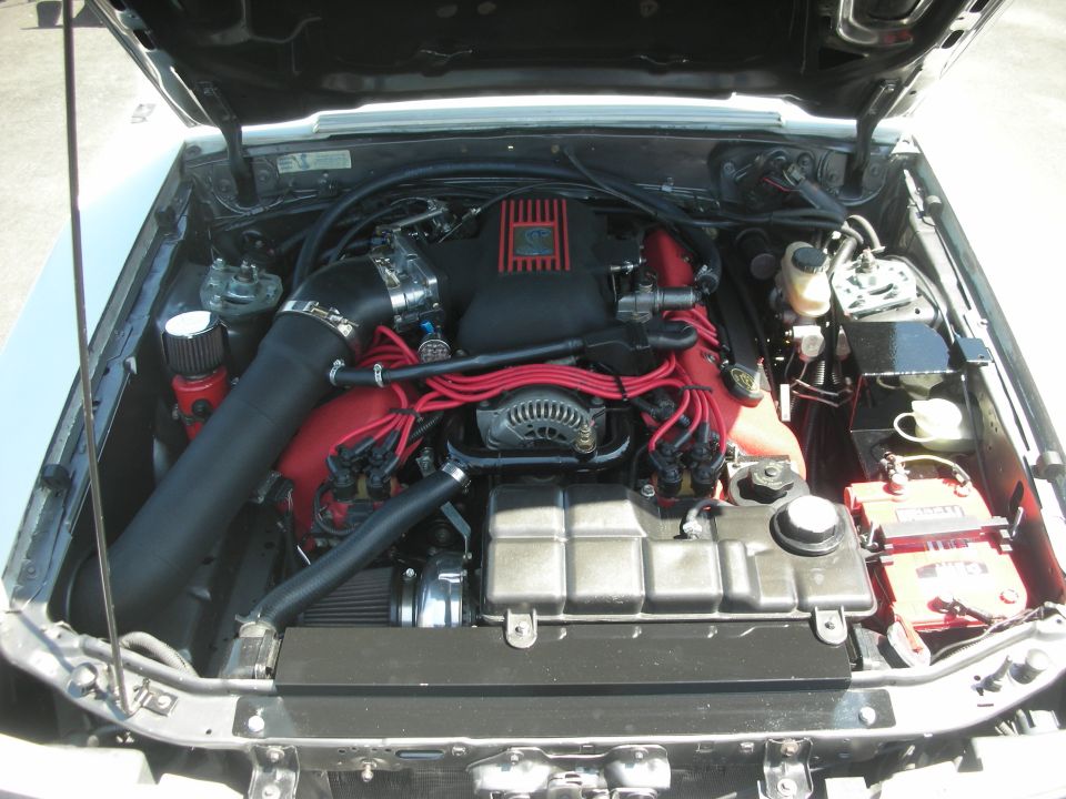 Engine bay with red and black components, aftermarket intake, and a V8 engine
