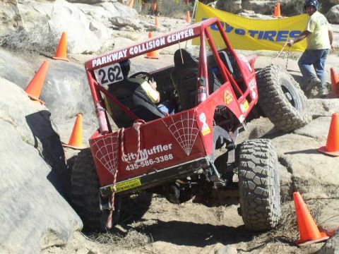 1979 Ford Bronco - A red off-road buggy, marked with number 262 and "City Muffler", tackles a challenging rocky terrain during an event.