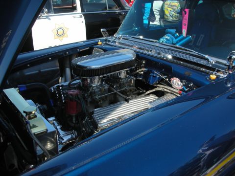 2004 Ford Crown Victoria - The engine bay of a blue car is shown, with a police car in the background.