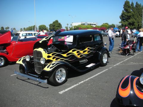 2004 Ford Crown Victoria - A black hot rod with flame graphics is parked at an outdoor car show next to a red convertible.