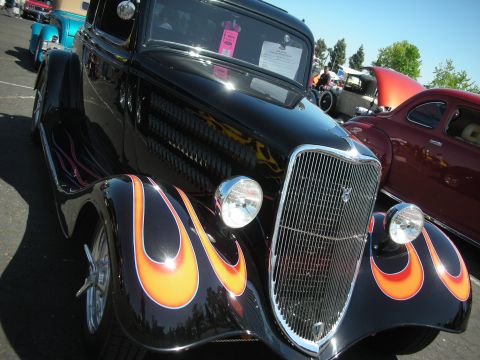 2004 Ford Crown Victoria - A black hot rod with flame decals is parked at a car show next to other vehicles.