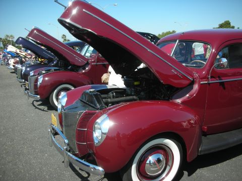 2004 Ford Crown Victoria - A line of vintage Ford coupes, including a maroon 1939 model, are displayed with their hoods open at an outdoor car show.