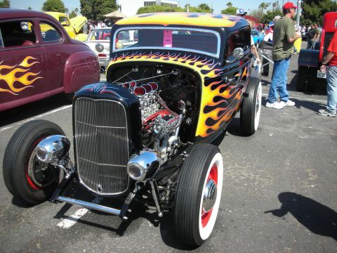 2004 Ford Crown Victoria - A custom hot rod with a flame paint job and exposed engine is parked next to another classic car at an outdoor event.