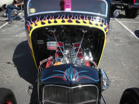 2004 Ford Crown Victoria - A hot rod with flames and pinstripes is displayed with its hood open, revealing the engine.