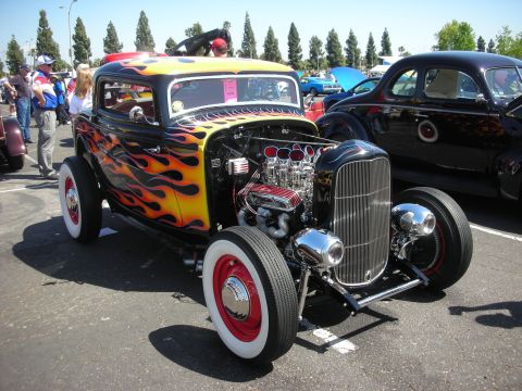 2004 Ford Crown Victoria - A black hot rod with yellow and orange flames, a chrome grille, and whitewall tires is parked at an outdoor car show.