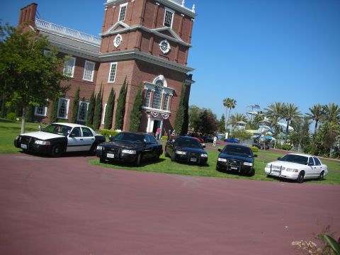2004 Ford Crown Victoria - Several police sedans, including a 2004 Ford Crown Victoria, are parked outside a brick building on a sunny day.