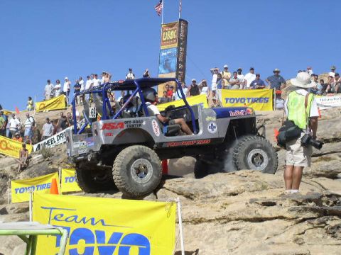 1979 Ford Bronco - A modified Jeep navigates a rocky course during an off-road competition with spectators in the background.