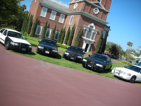 2004 Ford Crown Victoria - Multiple Ford Crown Victoria police cars are parked on the lawn in front of a large brick building.