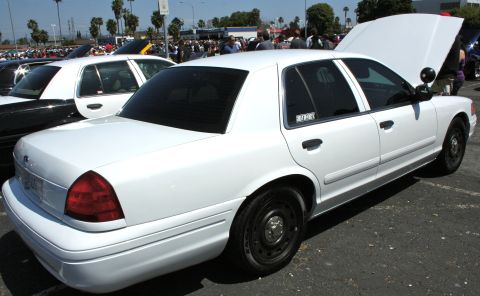 2004 Ford Crown Victoria - A white 2004 Ford Crown Victoria police car is displayed with its hood open at an outdoor car show.