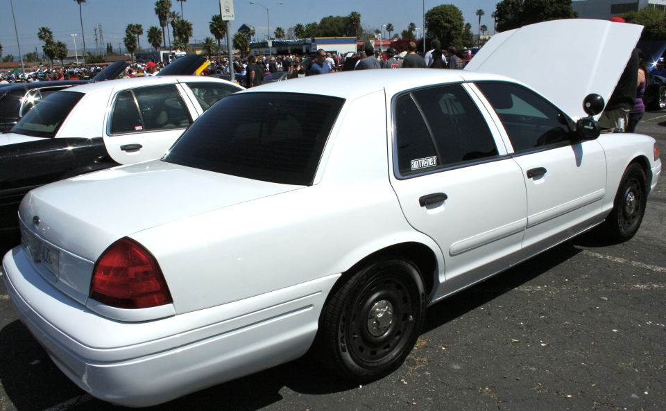 White 2004 Ford Crown Victoria police car, hood up, parked at an outdoor event