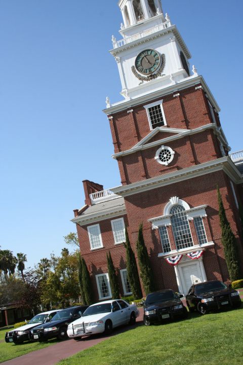 2004 Ford Crown Victoria - Several Ford Crown Victoria police cars are lined up on a grassy area in front of a large brick building with a prominent clock tower.
