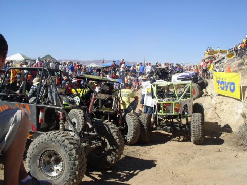 1979 Ford Bronco - Multiple custom off-road vehicles are lined up at a race event with spectators watching from the sidelines and a Toyo banner visible.