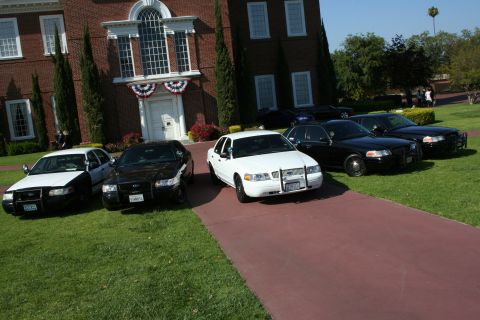 2004 Ford Crown Victoria - Several Ford Crown Victoria police cars are parked on the grass and driveway in front of a brick building.