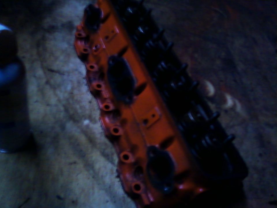 Cast-iron cylinder head freshly painted orange resting on a dim shop floor