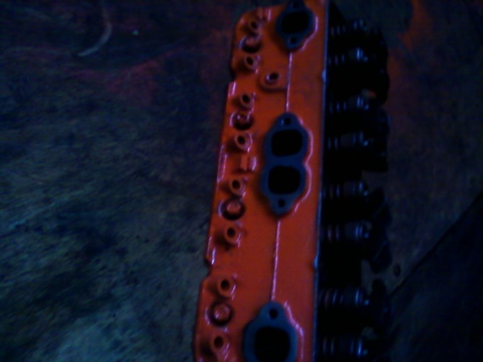 Orange engine part with black gaskets and visible valve springs