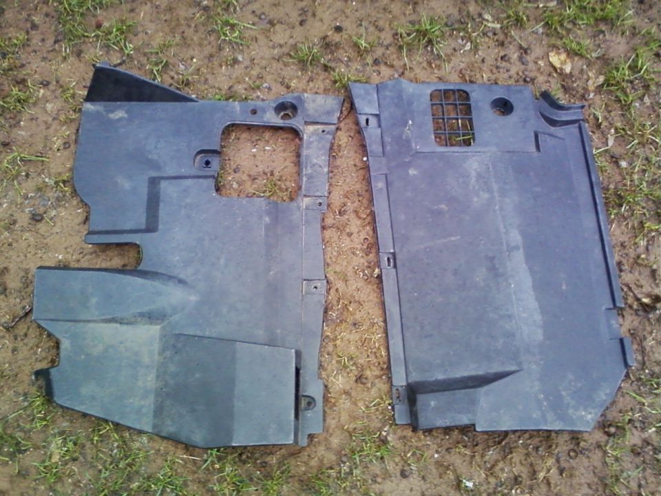 Pair of black molded plastic engine bay deflector panels lying on grass and dirt