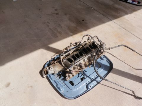 1982 Ford Bronco - Engine part on a blue tray on concrete with shadows.