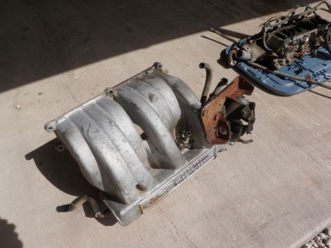 1982 Ford Bronco - Engine parts, including an aluminum intake manifold, are laid out on a concrete surface.