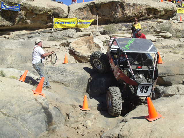 Off-road buggy with number 49 on a rocky course, a person is winching it