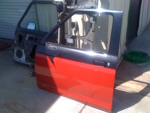 1992 Ford Ranger - A detached truck door, painted red and black, lies on a concrete surface next to a coiled green hose.