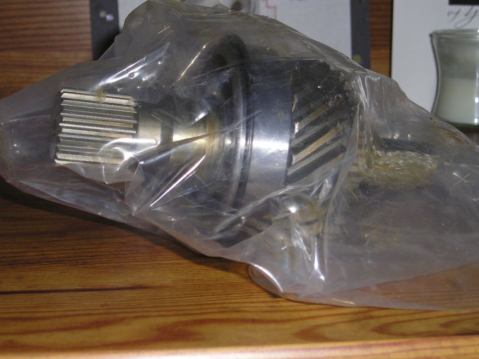 Metal gear with splines, wrapped in clear plastic, on a wooden surface