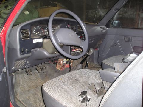 1990 Toyota Pickup/SR5 - The interior of a 1990 Toyota Pickup/SR5 shows plaid seats, a manual transmission, and the dashboard with a Toyota logo.